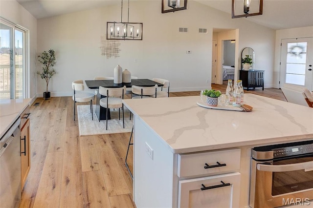 kitchen featuring lofted ceiling, stainless steel appliances, light wood-type flooring, light stone countertops, and a center island