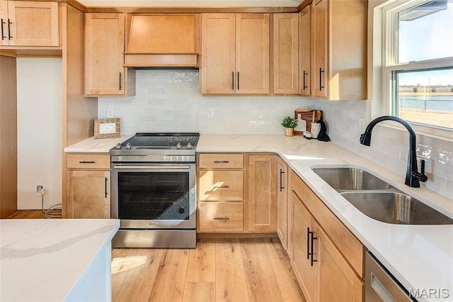 kitchen with appliances with stainless steel finishes, a sink, tasteful backsplash, light wood-style flooring, and light stone counters