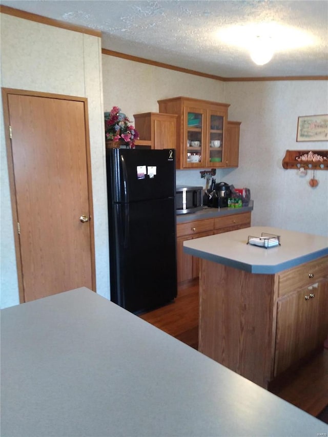 kitchen with freestanding refrigerator, brown cabinetry, stainless steel microwave, ornamental molding, and glass insert cabinets