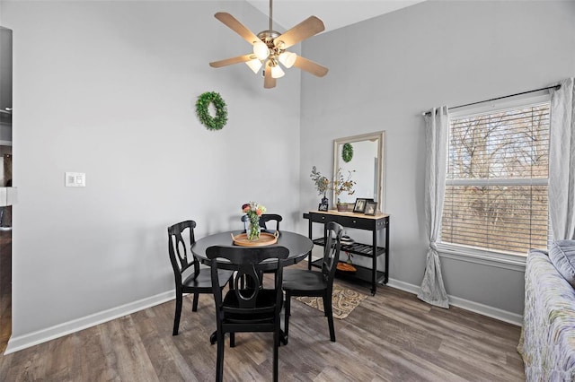 dining area with ceiling fan, wood finished floors, baseboards, and a towering ceiling