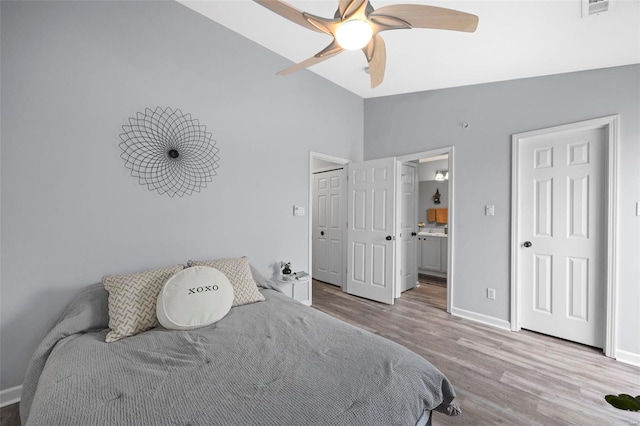 bedroom with wood finished floors, vaulted ceiling, baseboards, ensuite bathroom, and ceiling fan