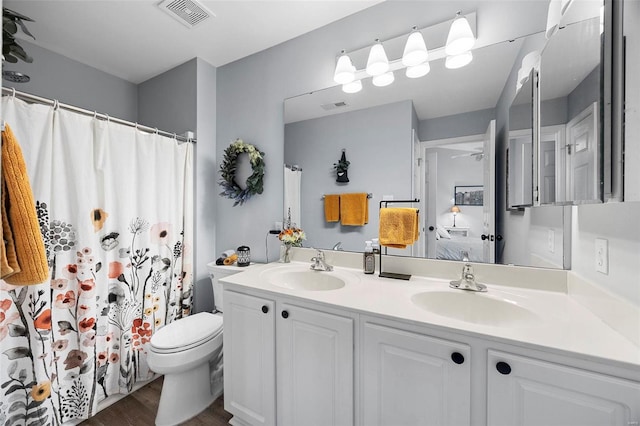 full bath with wood finished floors, double vanity, toilet, a ceiling fan, and ensuite bath