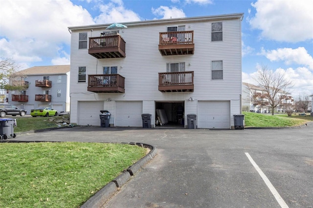 rear view of house featuring an attached garage, a yard, a balcony, and driveway
