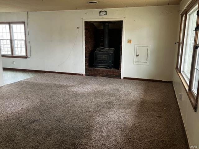 unfurnished living room with healthy amount of natural light, carpet floors, a wood stove, and baseboards