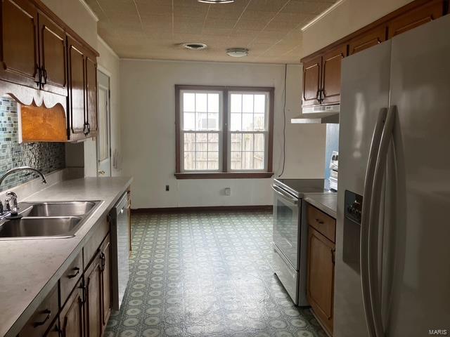 kitchen featuring stainless steel appliances, a sink, under cabinet range hood, backsplash, and light floors