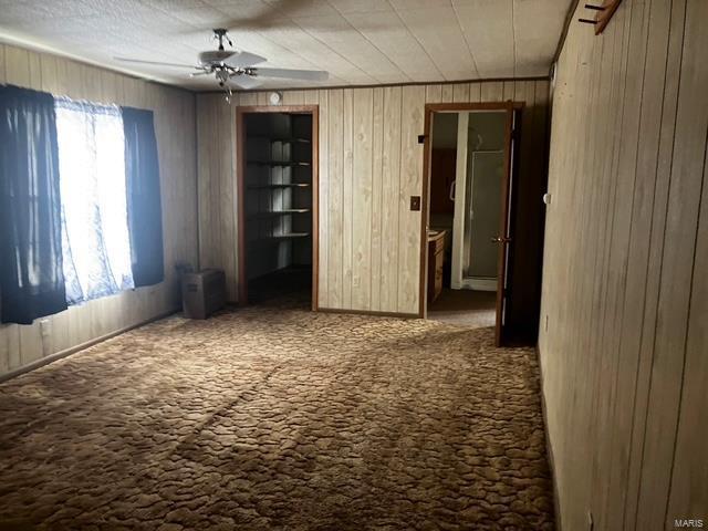 unfurnished bedroom with carpet floors, wooden walls, and a ceiling fan