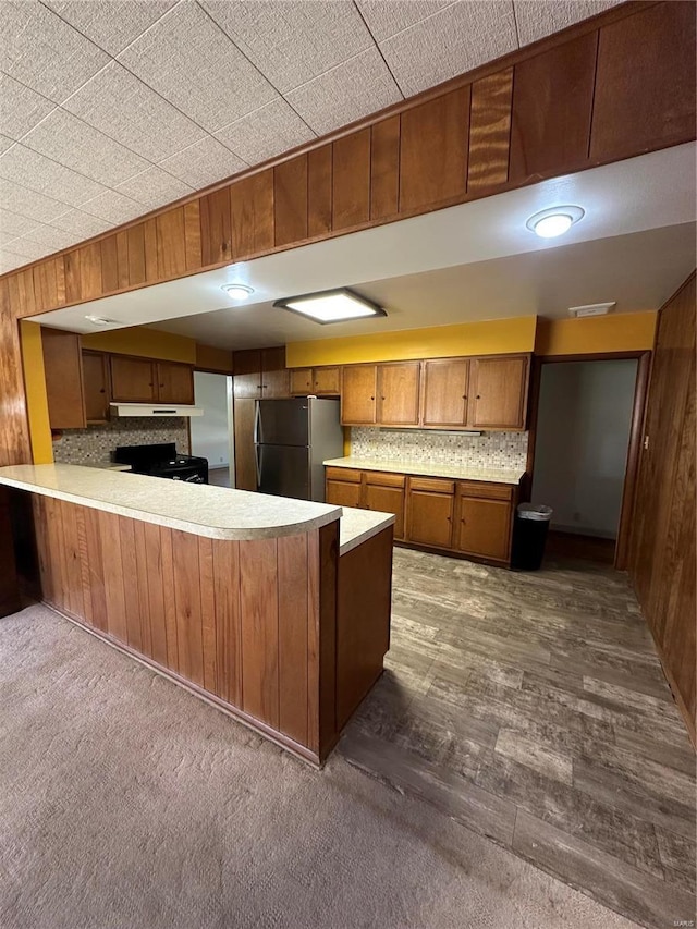 kitchen with freestanding refrigerator, brown cabinets, light countertops, a peninsula, and wood walls