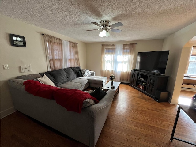 living area featuring healthy amount of natural light, arched walkways, ceiling fan, wood finished floors, and a textured ceiling