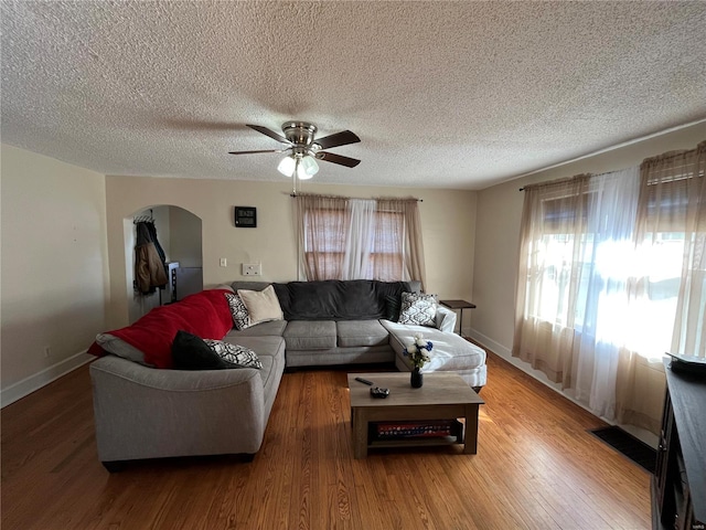 living room with ceiling fan, arched walkways, wood finished floors, baseboards, and a textured ceiling