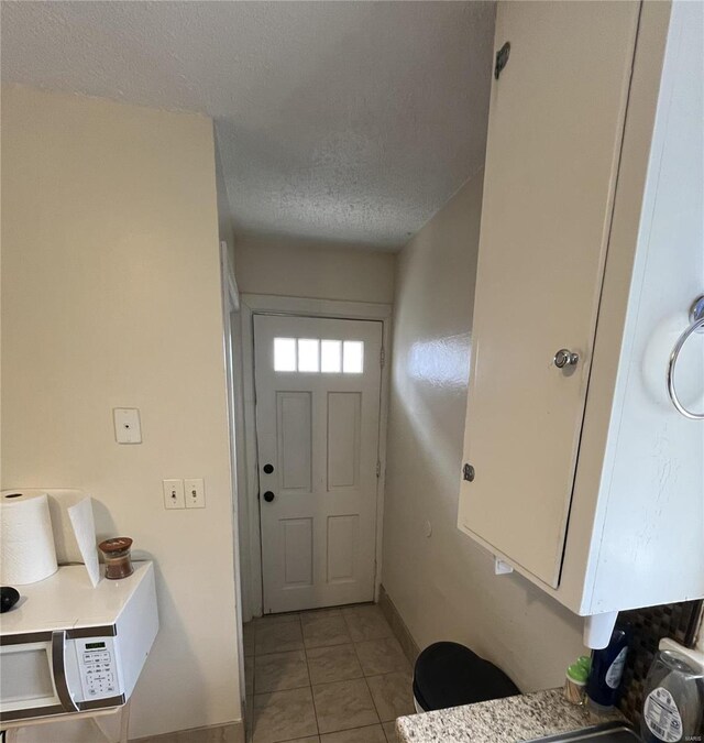 entryway with a textured ceiling, light tile patterned floors, and baseboards