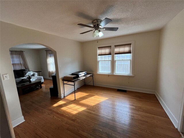 unfurnished room featuring arched walkways, ceiling fan, wood finished floors, a textured ceiling, and baseboards