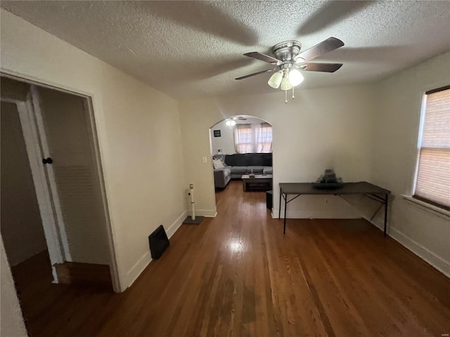 hall featuring arched walkways, wood finished floors, a textured ceiling, plenty of natural light, and baseboards