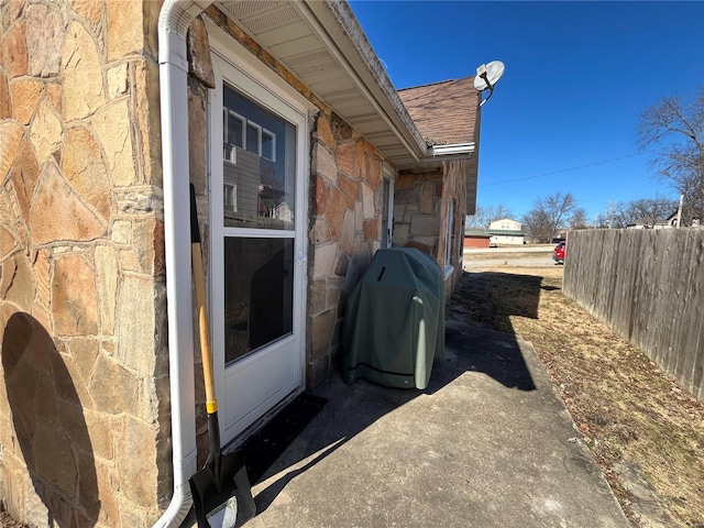 view of property exterior with stone siding, roof with shingles, and fence