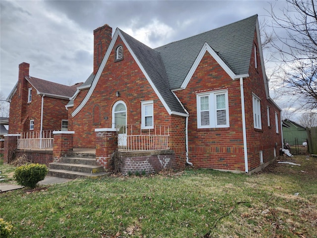 tudor home featuring a chimney, brick siding, a front yard, and roof with shingles