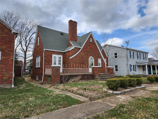 back of house with brick siding, a chimney, a yard, and roof with shingles