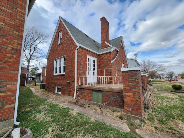 view of home's exterior featuring a chimney, brick siding, a shingled roof, and central AC