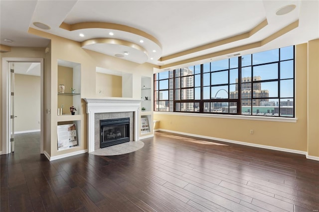 unfurnished living room with a tray ceiling, baseboards, a tile fireplace, and recessed lighting