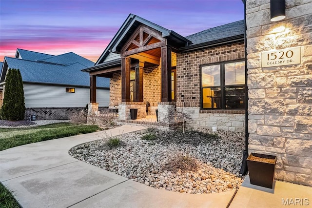 1520 Oglesby Dr, Edwardsville, IL 62025 - exterior entry at dusk featuring stone siding, brick siding, and a shingled roof