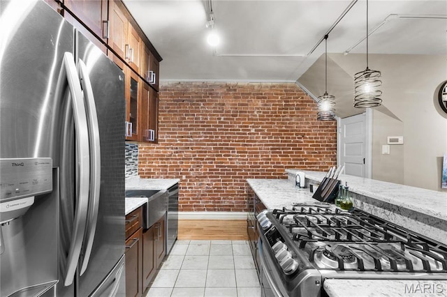 4486 Laclede Ave Unit 4486, Saint Louis, MO 63108 - kitchen with appliances with stainless steel finishes, brick wall, light stone countertops, light tile patterned floors, and hanging light fixtures