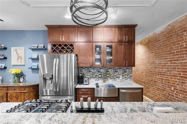 4486 Laclede Ave Unit 4486, Saint Louis, MO 63108 - kitchen featuring appliances with stainless steel finishes, a sink, glass insert cabinets, light stone counters, and brick wall