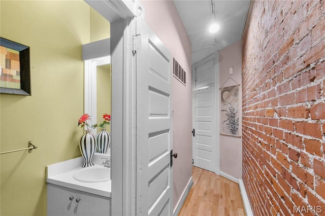 4486 Laclede Ave Unit 4486, Saint Louis, MO 63108 - bathroom featuring vanity, brick wall, and wood finished floors