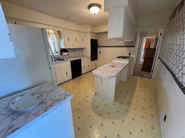 kitchen with black dishwasher, freestanding refrigerator, wallpapered walls, a sink, and light countertops