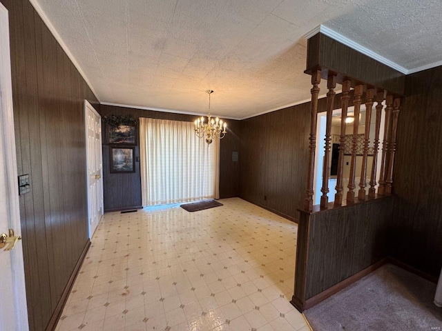 unfurnished dining area featuring tile patterned floors, wooden walls, ornamental molding, a chandelier, and baseboards