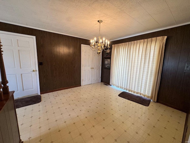 unfurnished dining area with light floors, a chandelier, wood walls, baseboards, and ornamental molding