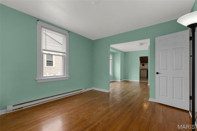 unfurnished room featuring a baseboard heating unit, healthy amount of natural light, wood finished floors, and baseboards