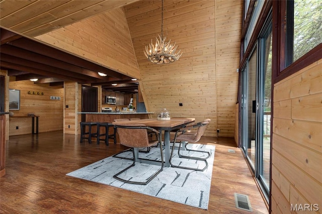 dining room with wooden walls, a chandelier, a high ceiling, and wood finished floors