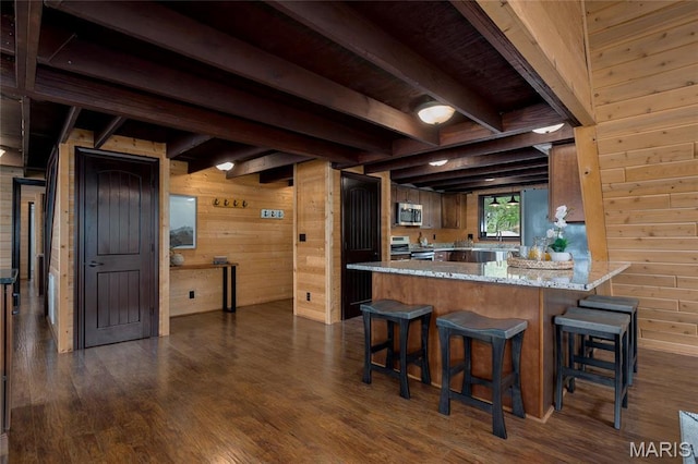 kitchen with stainless steel appliances, wooden walls, beam ceiling, dark wood finished floors, and a breakfast bar area