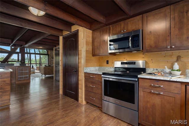 kitchen featuring stainless steel appliances, beam ceiling, dark wood-style flooring, wooden walls, and brown cabinets