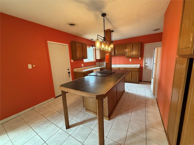 1227 Teson Rd, Hazelwood, MO 63042 - kitchen featuring tile counters, freestanding refrigerator, a kitchen island, decorative light fixtures, and brown cabinetry