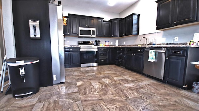 kitchen with appliances with stainless steel finishes, dark cabinetry, and a sink