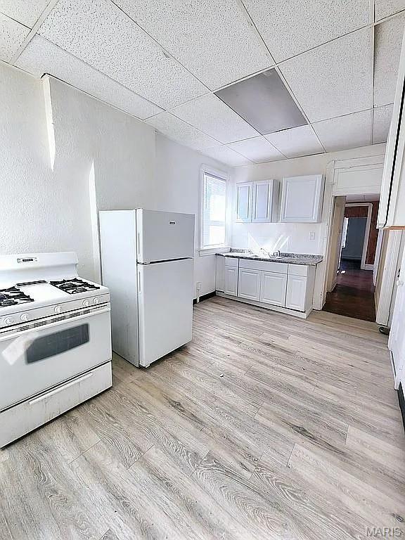 5244 Theodosia Ave, Saint Louis, MO 63113 - kitchen with white appliances, light wood-style flooring, a drop ceiling, and light countertops