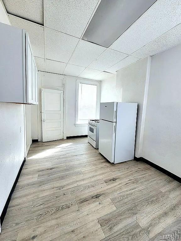 5244 Theodosia Ave, Saint Louis, MO 63113 - kitchen with white appliances, light wood-style flooring, baseboards, and a drop ceiling