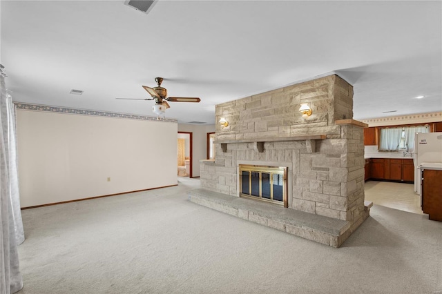 unfurnished living room with light carpet, ceiling fan, a fireplace, and baseboards