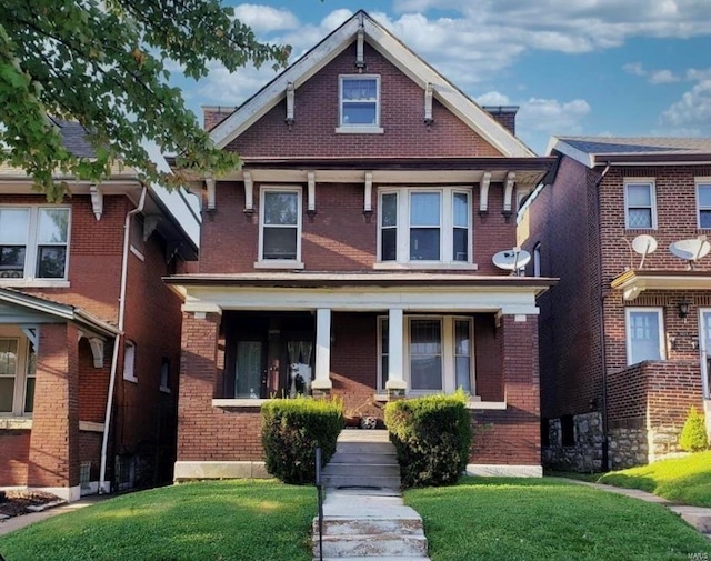 american foursquare style home with brick siding, a front yard, and covered porch
