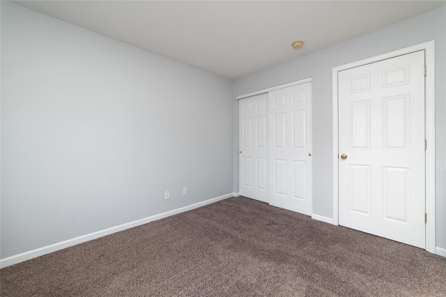 unfurnished bedroom featuring dark carpet, baseboards, and a closet