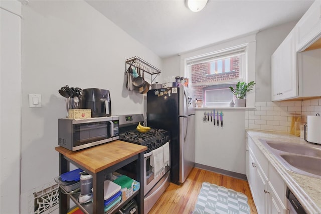 5044 Lindenwood Ave, Saint Louis, MO 63109 - kitchen with appliances with stainless steel finishes, light wood finished floors, white cabinets, decorative backsplash, and a sink