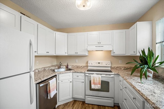 kitchen featuring white appliances, a sink, under cabinet range hood, white cabinets, and a textured ceiling