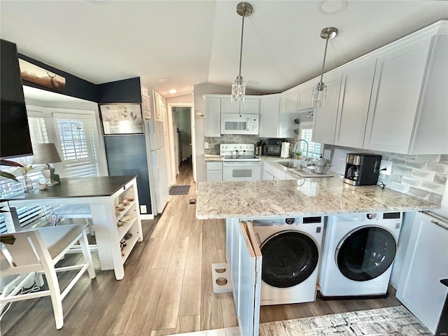 kitchen with white appliances, healthy amount of natural light, washer and dryer, a peninsula, and vaulted ceiling