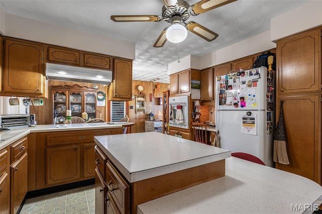 113 S Madison St, Desloge, MO 63601 - kitchen featuring freestanding refrigerator, oven, under cabinet range hood, brown cabinetry, and light countertops
