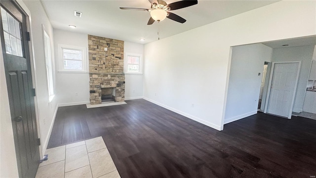 unfurnished living room featuring wood finished floors, ceiling fan, a stone fireplace, and baseboards