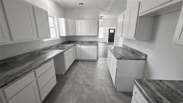 kitchen with plenty of natural light, dark stone counters, a sink, and white cabinets