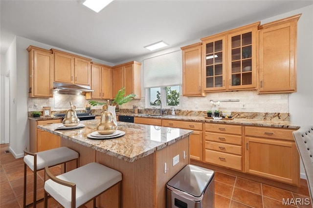 kitchen with a sink, a breakfast bar area, backsplash, light stone countertops, and a kitchen island
