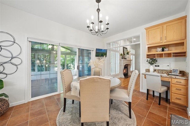 dining space featuring a warm lit fireplace, a chandelier, dark tile patterned flooring, and baseboards