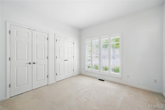 unfurnished bedroom with two closets, carpet floors, and baseboards