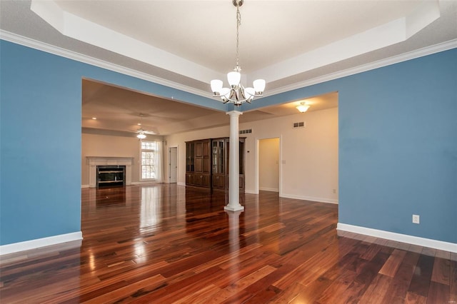 unfurnished living room featuring a raised ceiling, decorative columns, wood finished floors, a chandelier, and baseboards