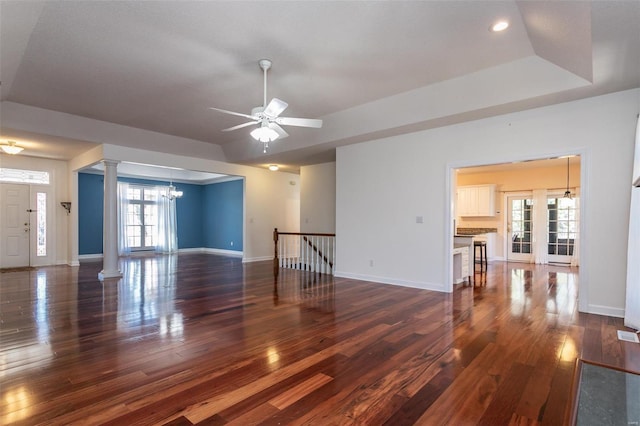 unfurnished living room featuring ornate columns, a chandelier, hardwood / wood-style floors, baseboards, and a ceiling fan